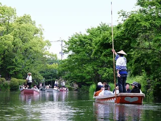 春日綠蔭下的柳川遊船，幾位船夫持長篙帶著旅人穿過掘割