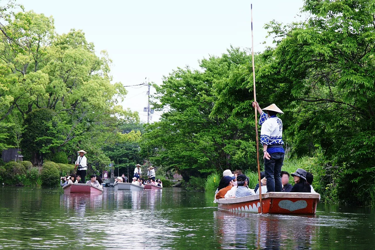 春日綠蔭下的柳川遊船，幾位船夫持長篙帶著旅人穿過掘割